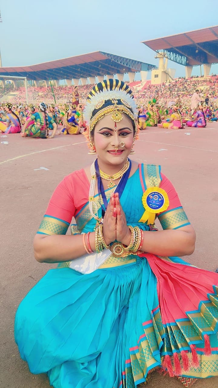 A dancer in turquoise and pink costume greeting the camera at a stadium gathering