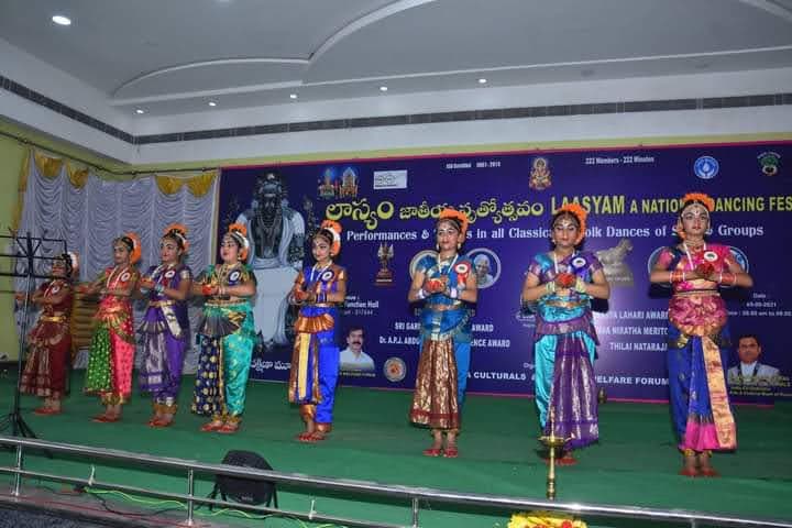 A line of dancers performing coordinated gestures on the Laasyam stage