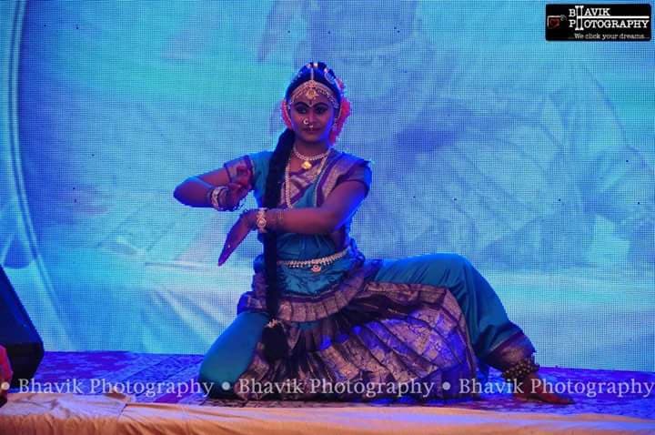 A solo classical dancer in a low expressive pose against a blue stage backdrop