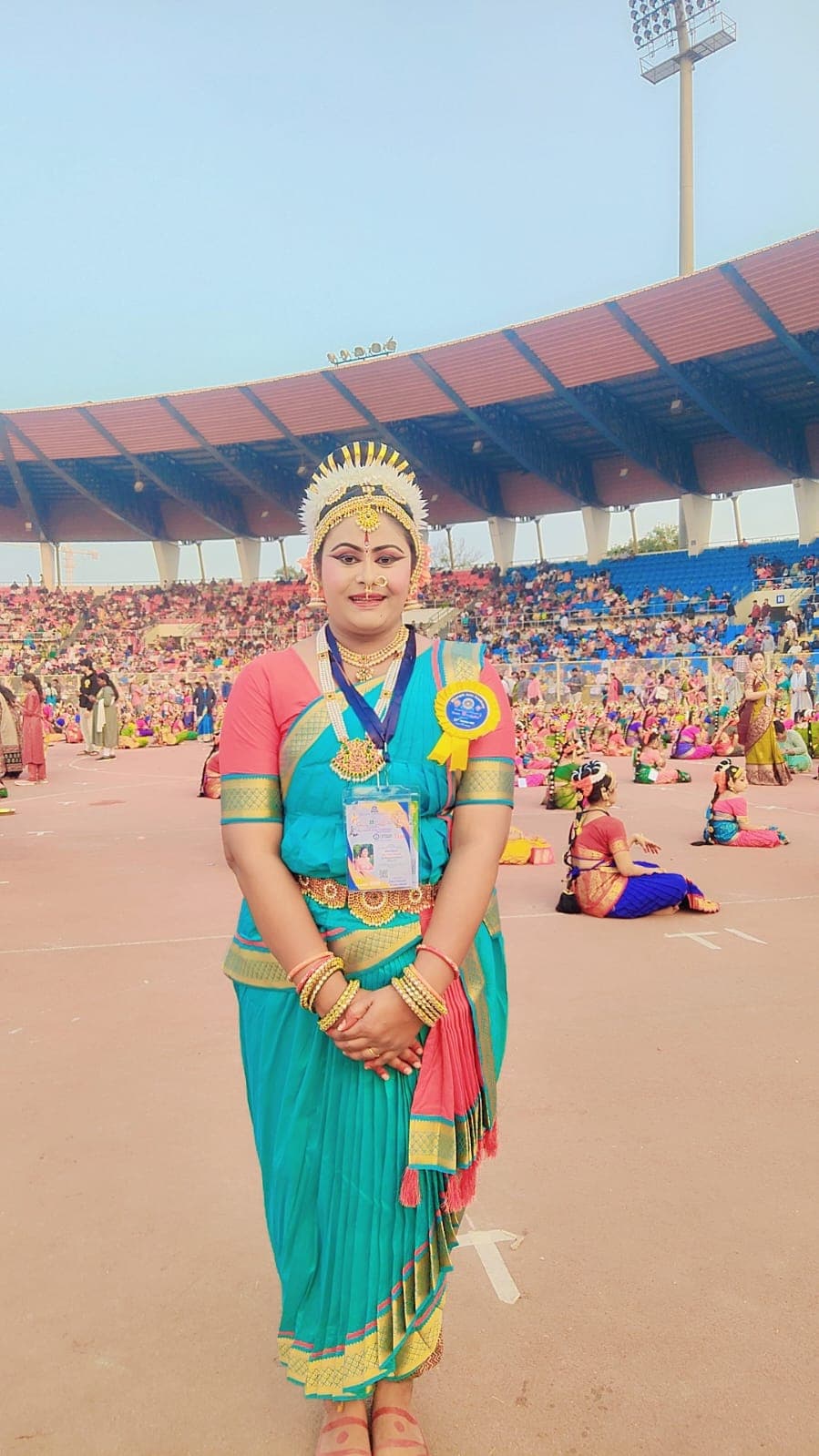 A dancer in turquoise costume standing in a stadium filled with participants