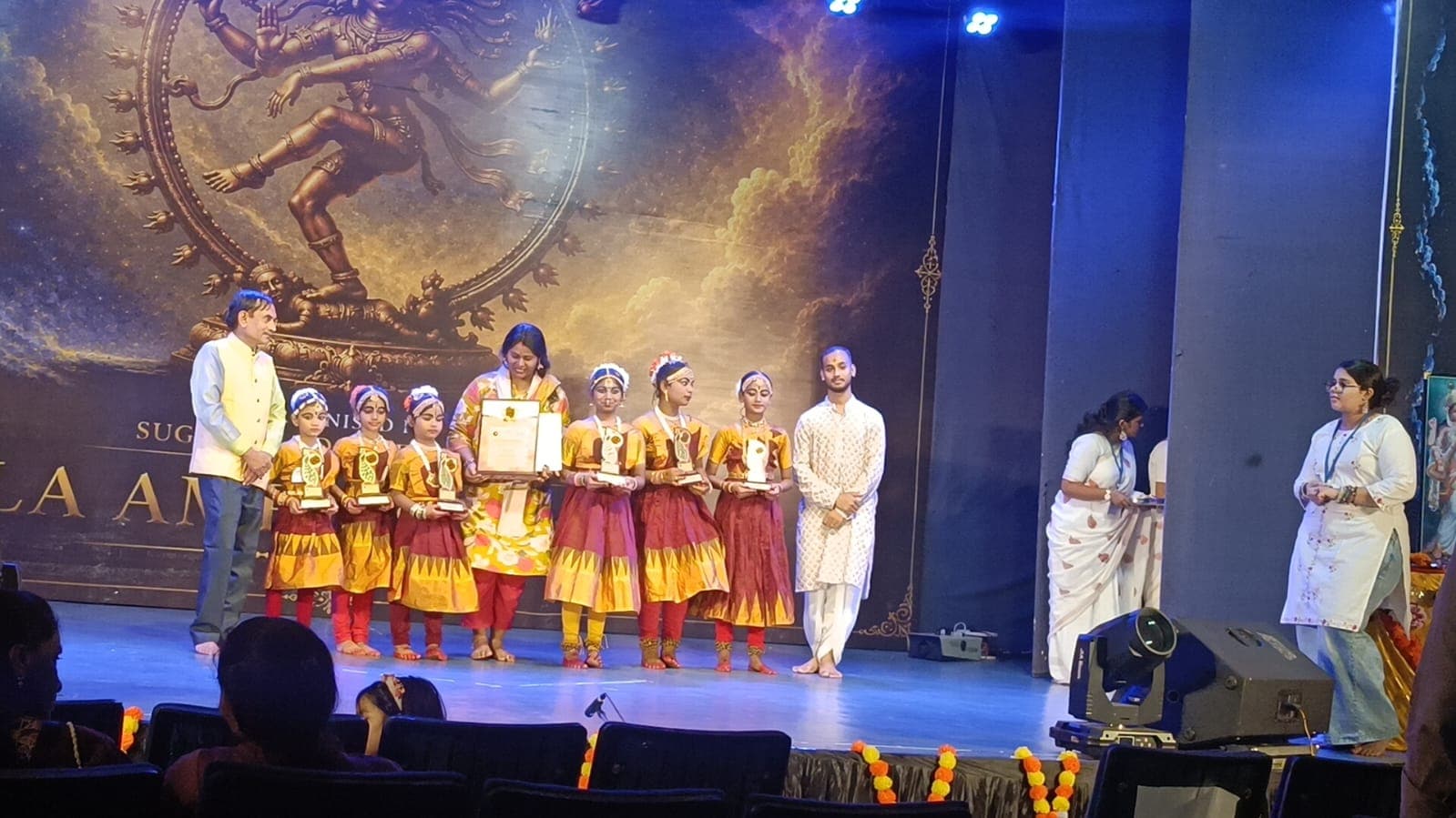 Young dancers receiving recognition on a blue-lit cultural stage