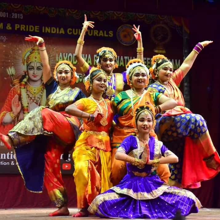 An ensemble of dancers holding expressive poses in colourful costumes