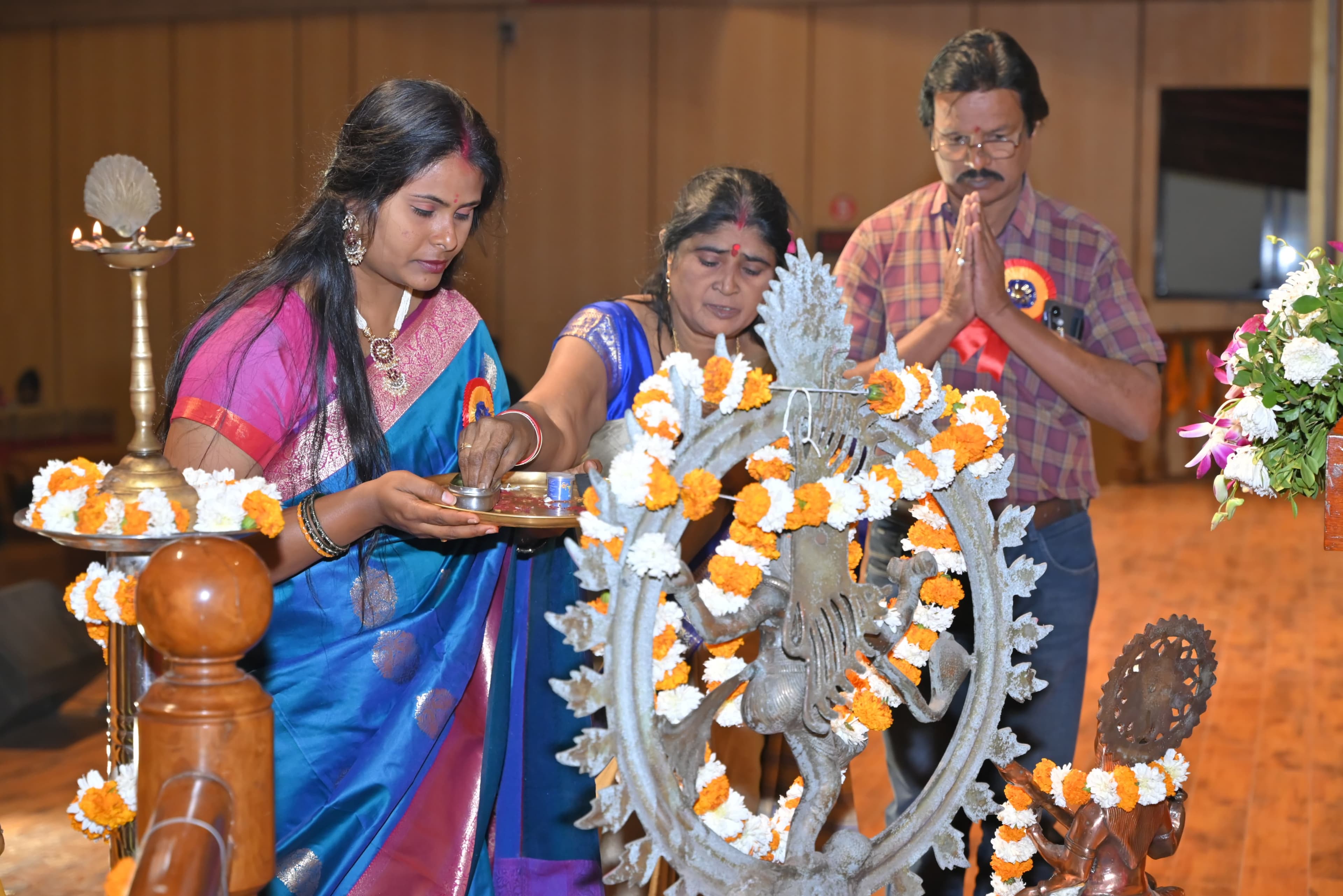 Guests lighting a ceremonial lamp beside a flower-decorated Nataraja sculpture